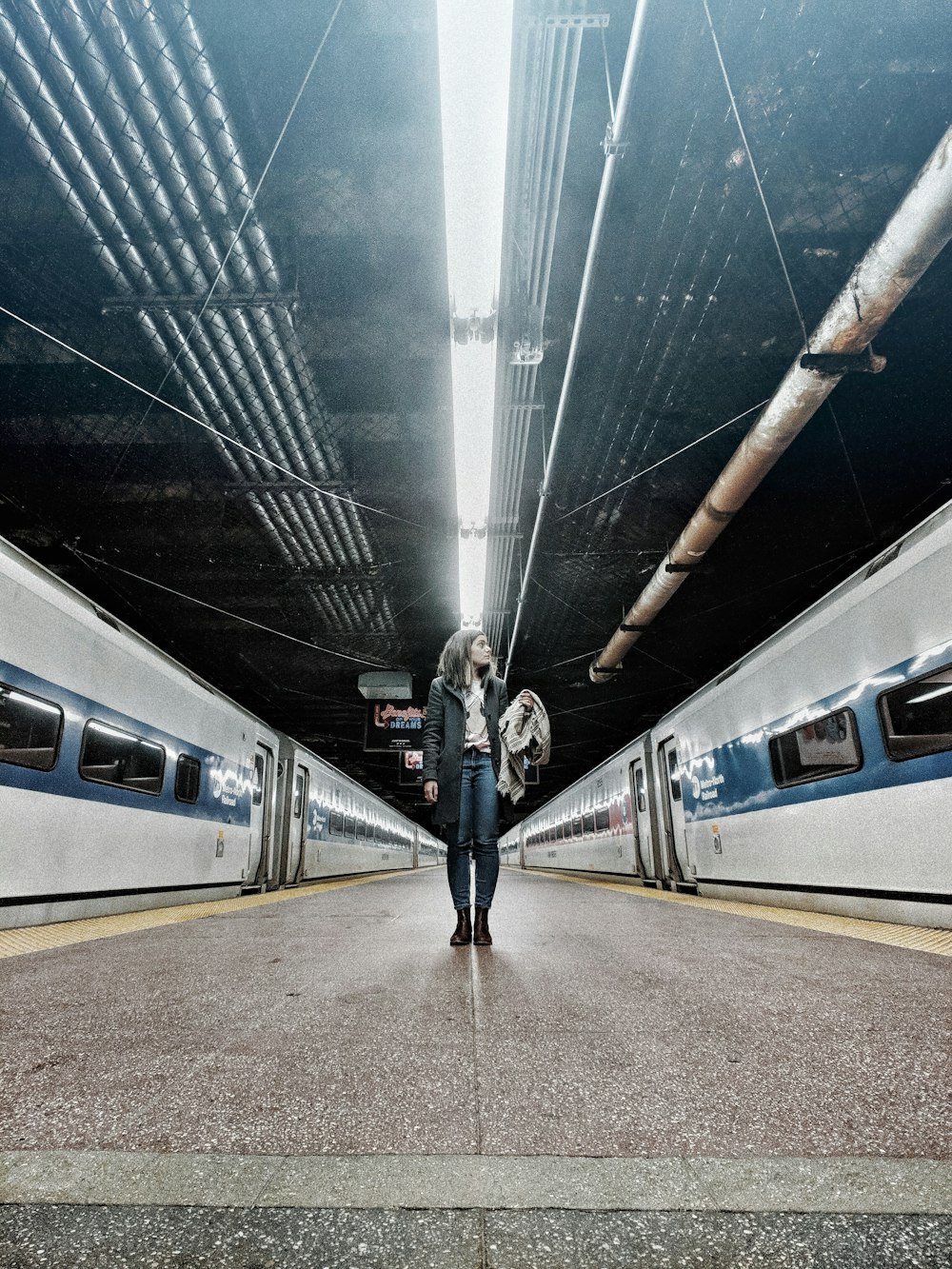 Donna in piedi nel mezzo dei treni grigi all'interno della stazione ferroviaria