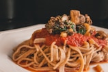 A plate of pasta with a thick layer of red tomato sauce, topped with mushrooms, spinach, and other vegetables. The pasta looks freshly cooked and the sauce is rich and vibrant, creating an appetizing presentation.