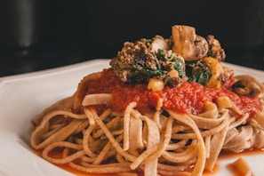 A plate of pasta with a thick layer of red tomato sauce, topped with mushrooms, spinach, and other vegetables. The pasta looks freshly cooked and the sauce is rich and vibrant, creating an appetizing presentation.