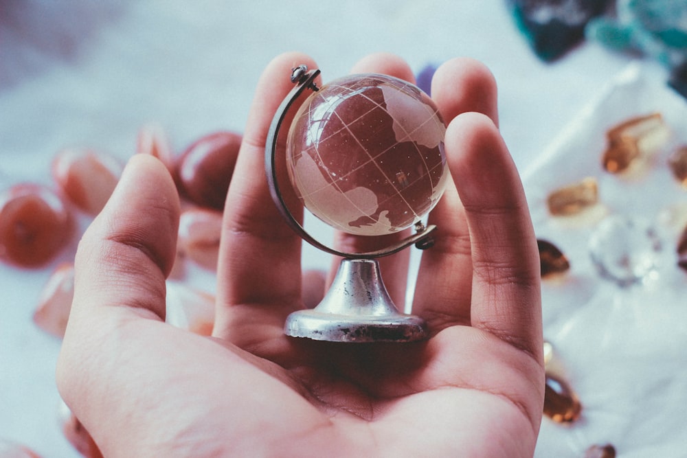 person holding gray metal framed desk globe paper weight