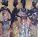 Four silhouetted women are adorned in vibrant, patterned dresses with matching head wraps, set against a textured background of warm tones and abstract designs. They stand in confident poses, highlighting their elegant attire and jewelry.