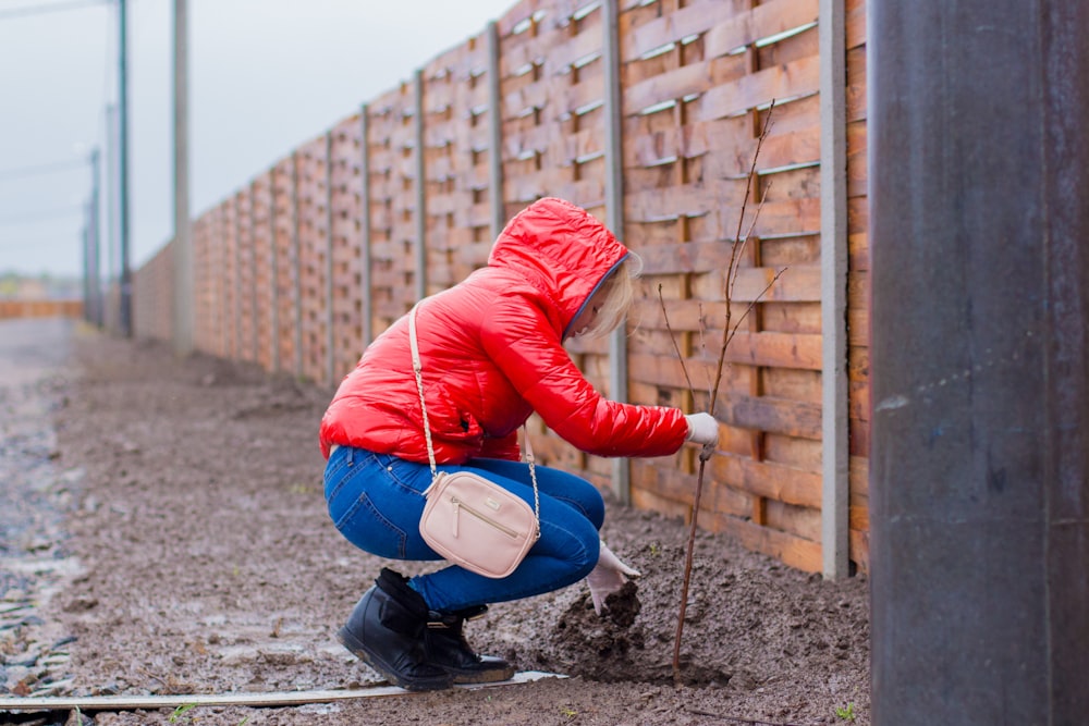 woman wearing red coat planting plant on mud