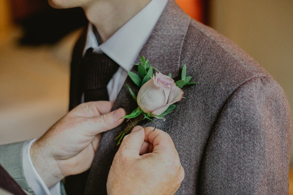 person putting pink rose pin on person's notched lapel suit jacket