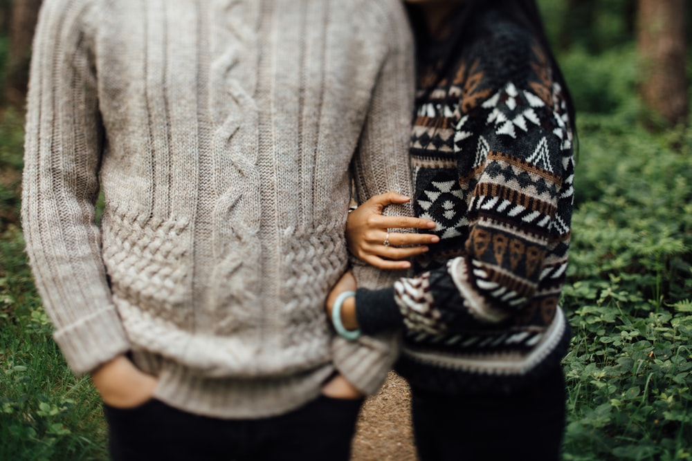 Femme en pull noir et blanc étreignant un homme en pull en tricot torsadé gris