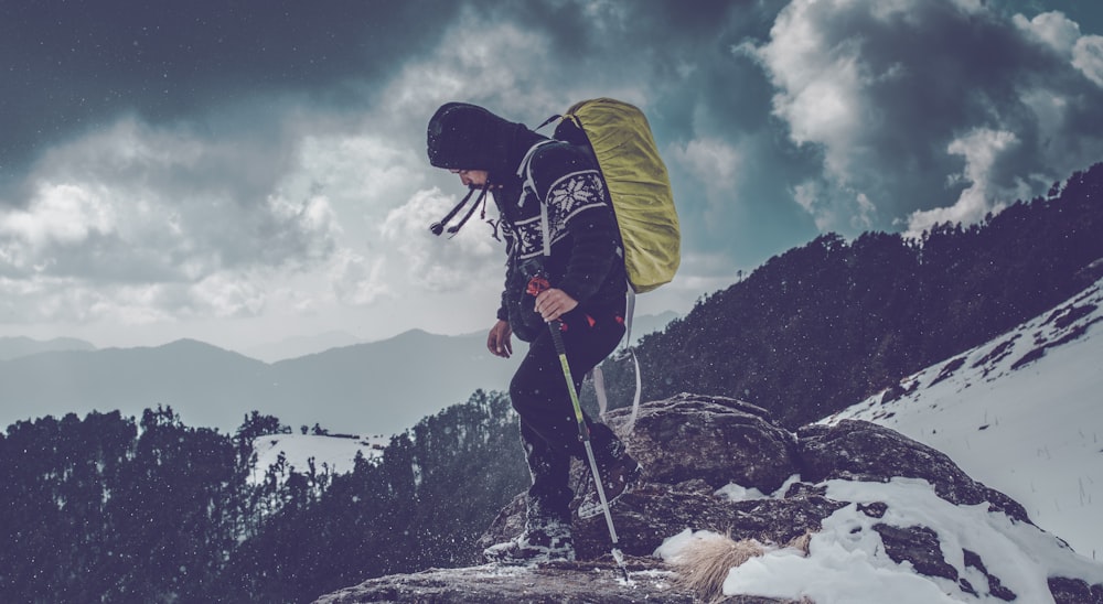 man carrying backpack standing on cliff near trees during daytime