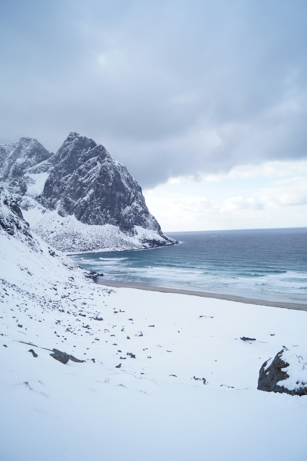 montañas cubiertas de nieve en la costa bajo el cielo gris