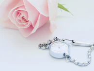 A soft pink rose beside a compact, stylish safety alarm resting on a light beige surface.
