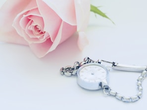 Delicate pink dial watch with matching pink milanese mesh strap placed beside fresh flowers.