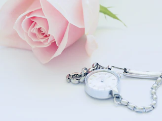 A soft pink rose beside a compact, stylish safety alarm resting on a light beige surface.