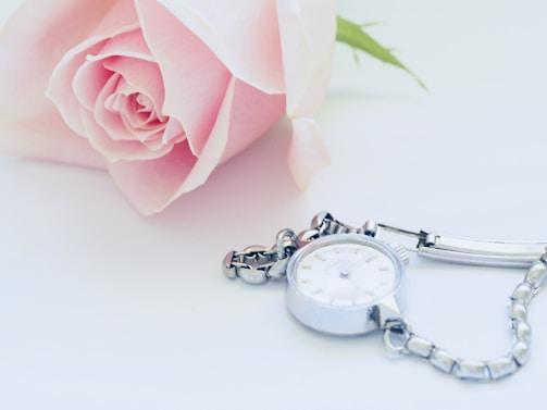 A close-up of a delicate women's watch resting beside a vintage letter and a soft pink rose.