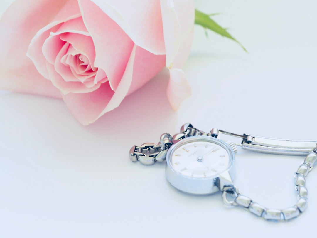 round white analog watch beside pink rose
