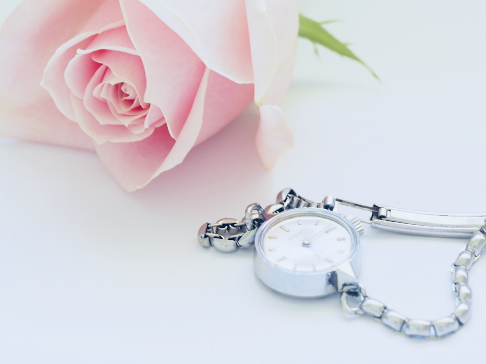 round white analog watch beside pink rose