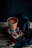 A bowl filled with rich cacao powder next to a spoon and panela blocks on a pastel-colored cloth.