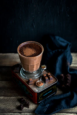 A bowl filled with rich cacao powder next to a spoon and panela blocks on a pastel-colored cloth.