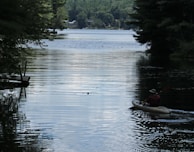 A family kayaking in a serene lake with trees reflecting on the water.