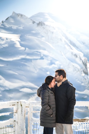 A couple enjoying a warm fire outside the cabin surrounded by snow-capped mountains.