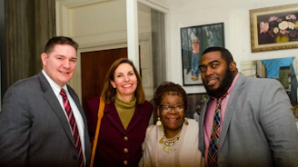 A warm group photo of four team members smiling and standing close together in a cozy workspace.