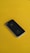 A black smartphone is resting on a bright yellow surface. The phone's back features a prominent silver apple logo, and its design is sleek and minimalist.