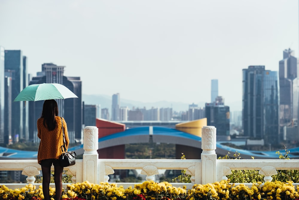 woman using blue umbrella standing in front of fence