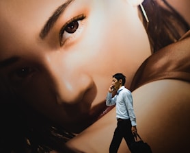 man walking while holding smartphone near woman-themed wall painting