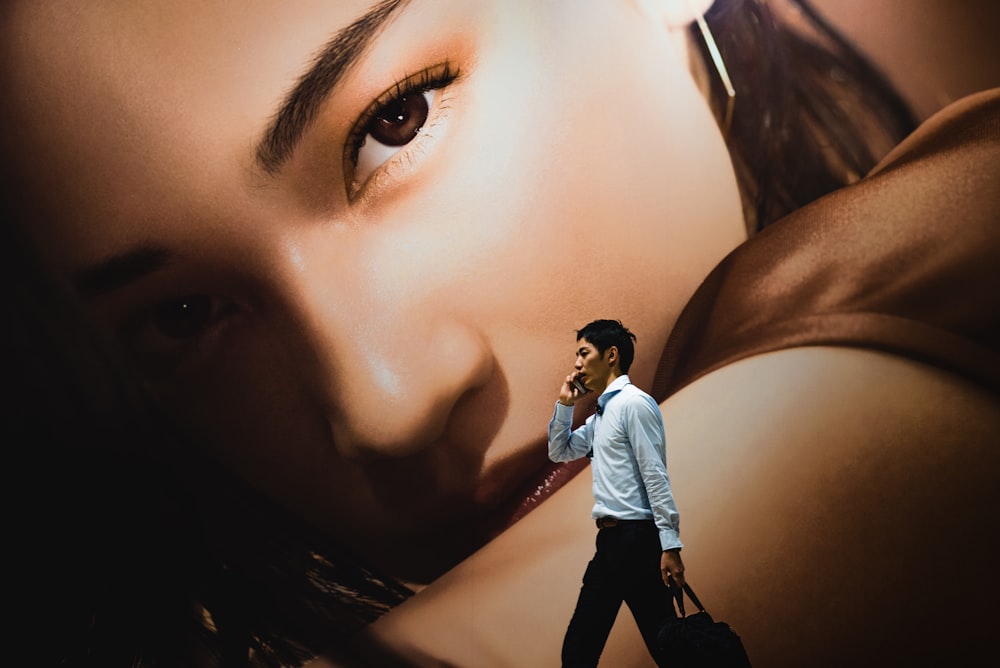 man walking while holding smartphone near woman-themed wall painting