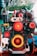 An industrial engine featuring prominent red and yellow pulleys is set against an outdoor environment. The intricate mechanical components are highlighted through vibrant colors, blending with the natural green backdrop.