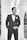 A man in a formal black suit and bow tie stands confidently with hands in pockets. The backdrop features classic architectural columns and arches, suggesting an elegant setting.