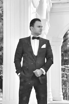 Man in sleek black suit with rose gold cufflinks standing confidently against minimalist backdrop.