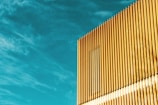 A modern building facade featuring vertical golden panels in strong sunlight, set against a vivid blue sky with sparse clouds.
