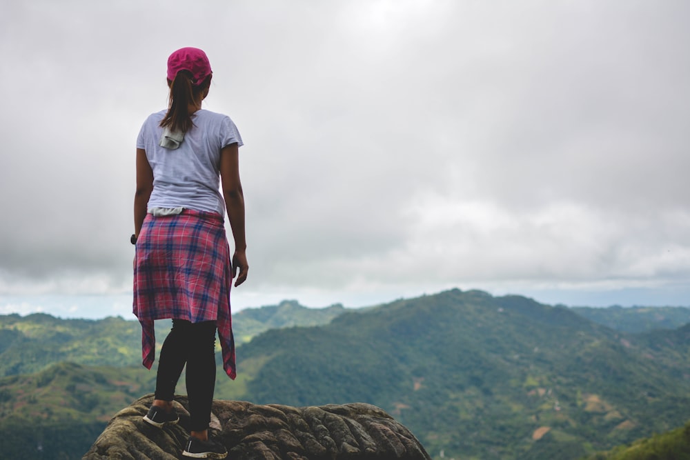 woman standing on mountain peak facing green mountains at daytime