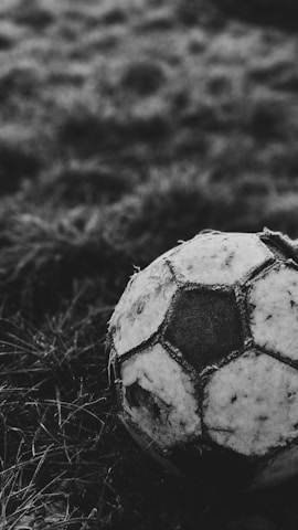 Close-up of a vintage soccer ball resting on the grass with a stadium in the background.