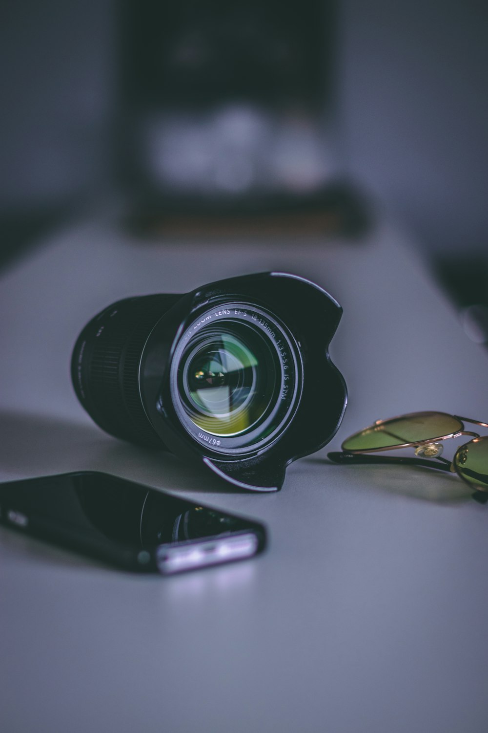 black telephoto lens beside smartphone and sunglasses