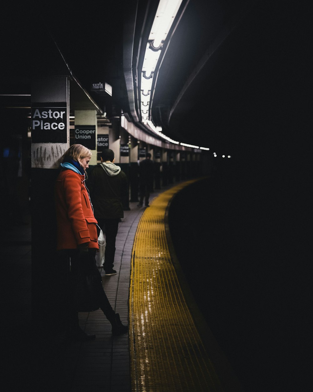 woman wearing red coat leaning on column on train station