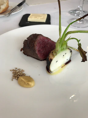 Close-up of a perfectly cooked medium-rare beef filet on a dark plate with herb butter and seasonal vegetables.
