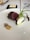 A gourmet dish featuring a piece of medium-rare meat and a root vegetable with charred greens on a white plate. Accompanied by a small dollop of mustard and some seeds. A slab of butter is on a square black dish in the background along with a piece of bread and cutlery.