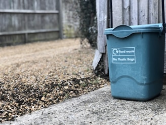 green food waste bin beside wooden fence
