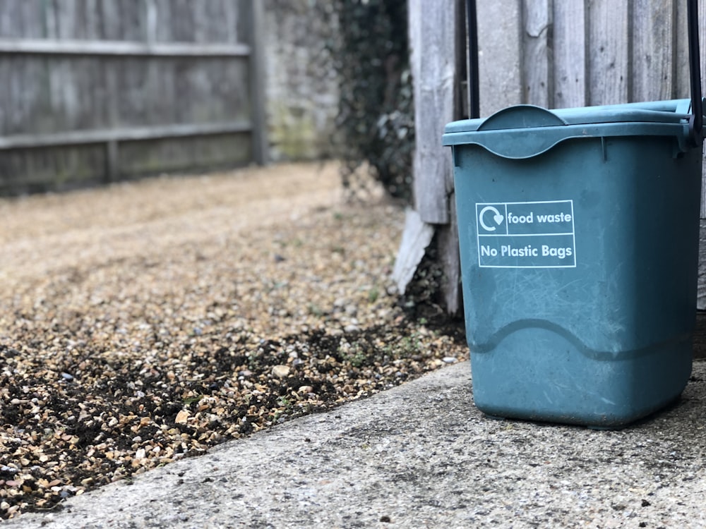 Cubo de basura verde al lado de la valla de madera