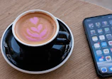 Close-up of a freshly brewed coffee cup with a mobile device showing a food delivery app.