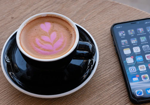 Close-up of a freshly brewed coffee cup with a mobile device showing a food delivery app.