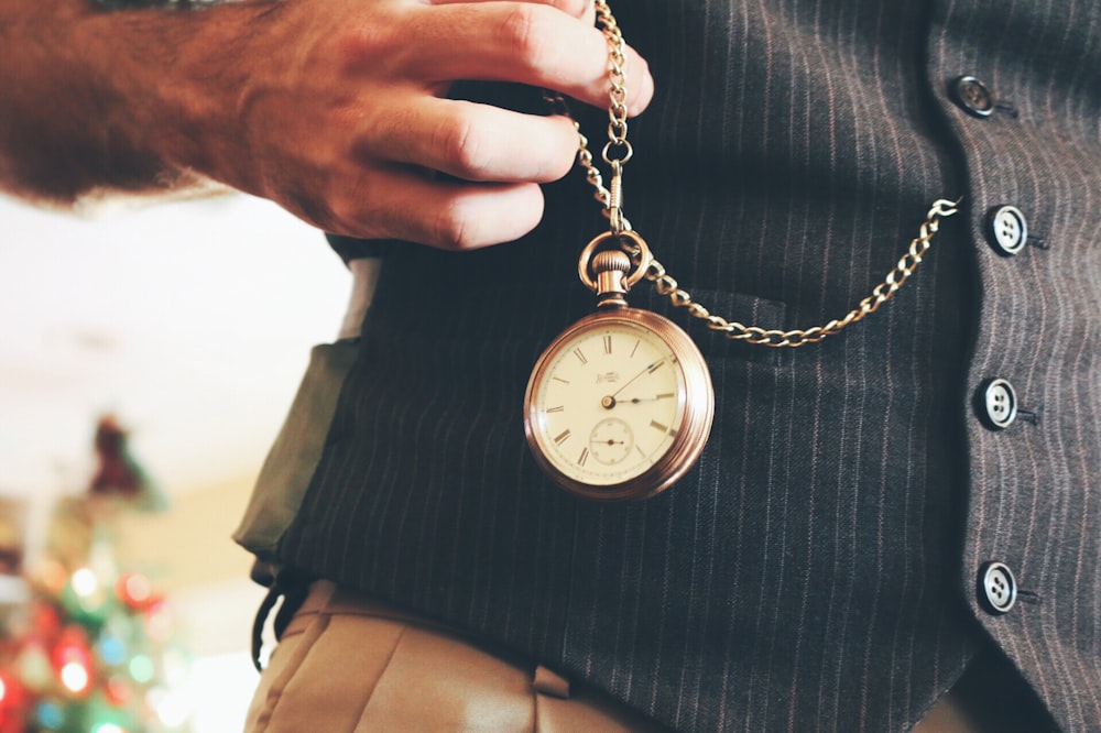 Persona sosteniendo un reloj de bolsillo redondo de color dorado