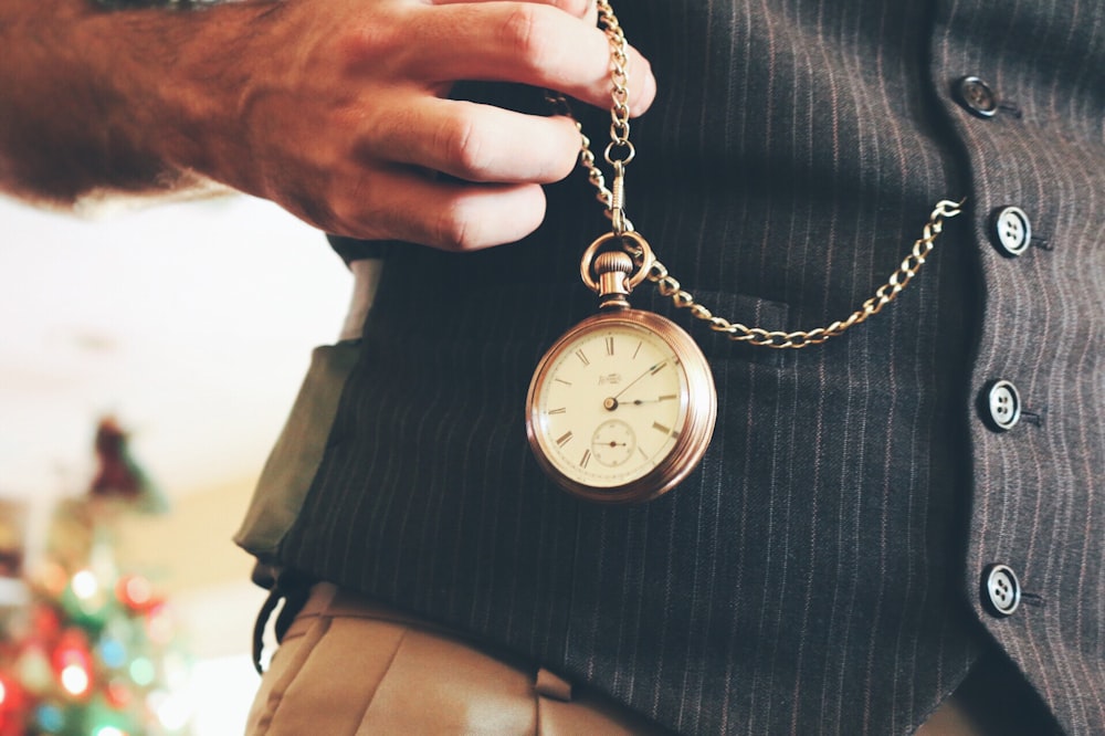 Persona che tiene in mano un orologio da tasca rotondo color oro