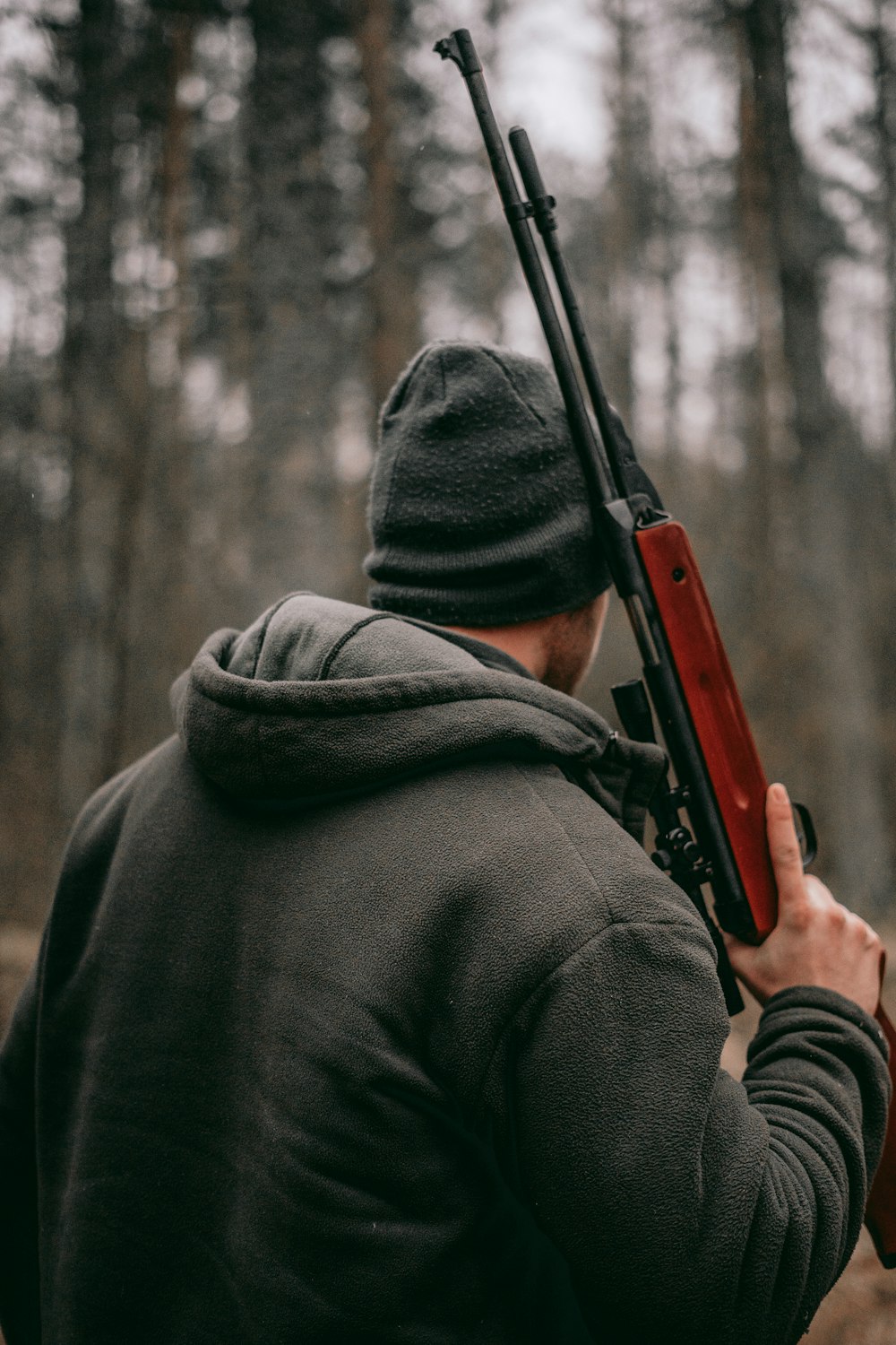 Homem segurando rifle de precisão marrom e preto em fotografia de foco raso