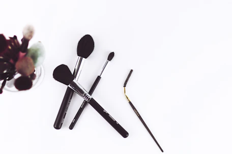 Minimalist arrangement of makeup brushes and palettes on a white surface with subtle shadows.