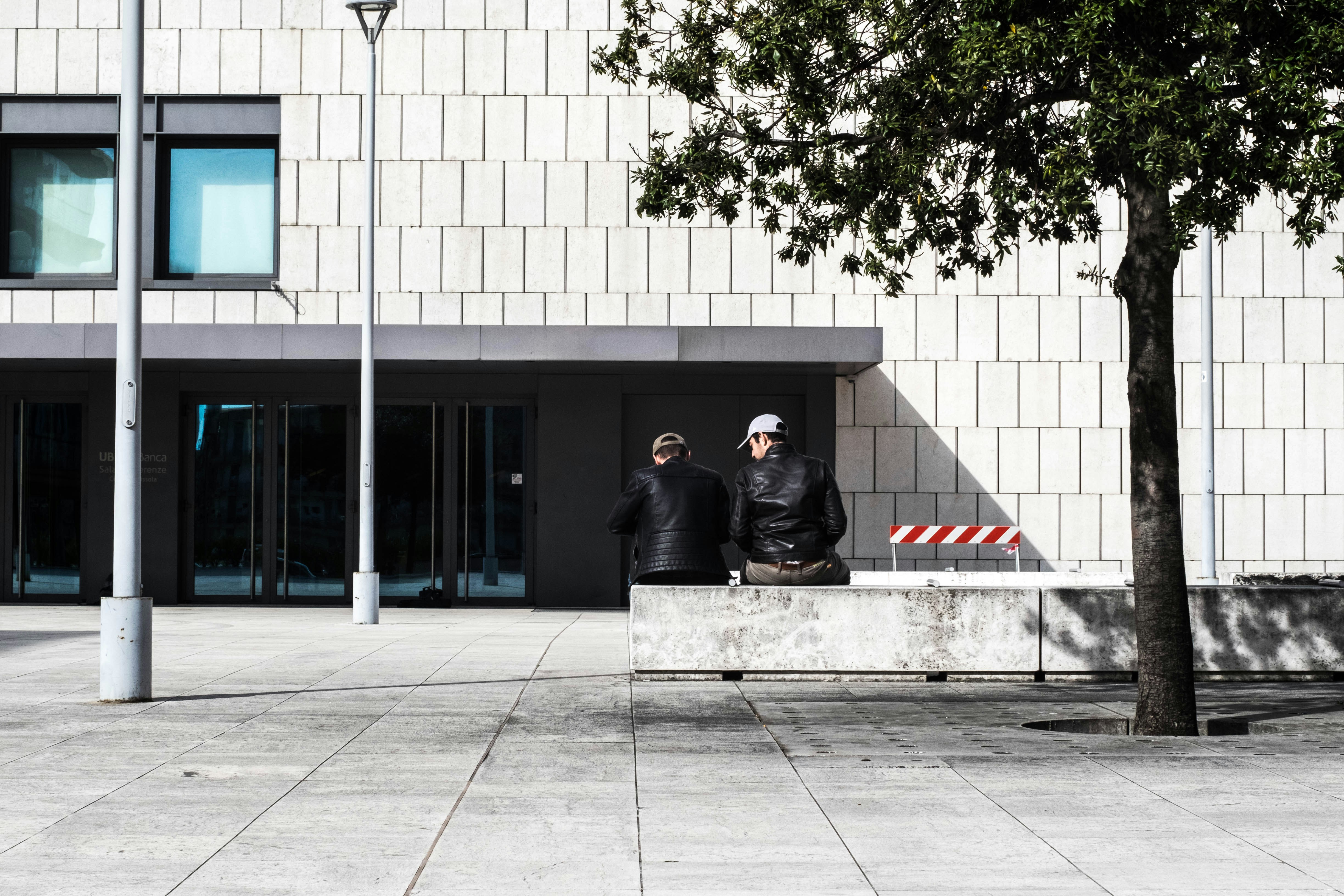 two men sitting on concrete barricade near store