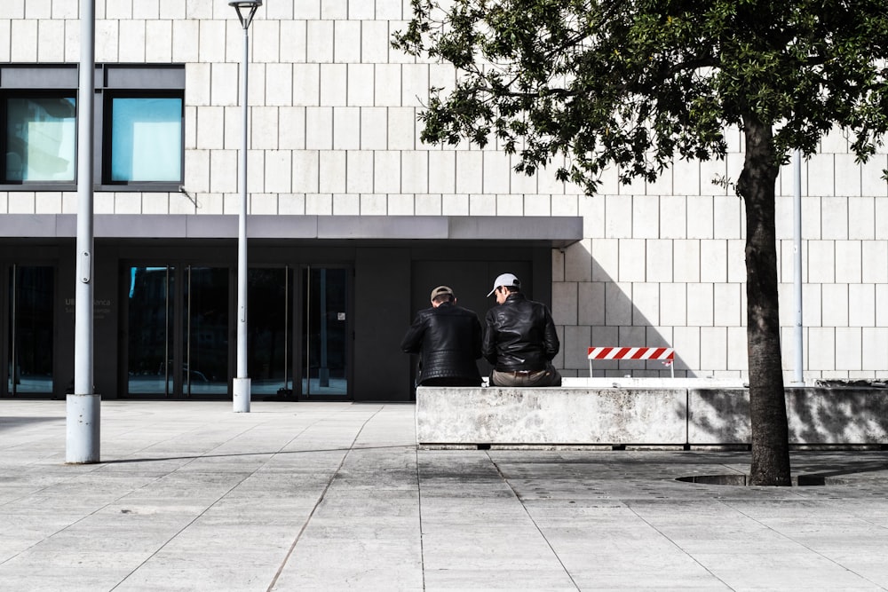 two men sitting on concrete barricade near store