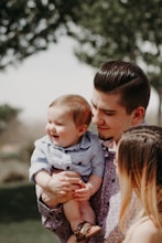 man carrying baby beside woman while smiling to each other