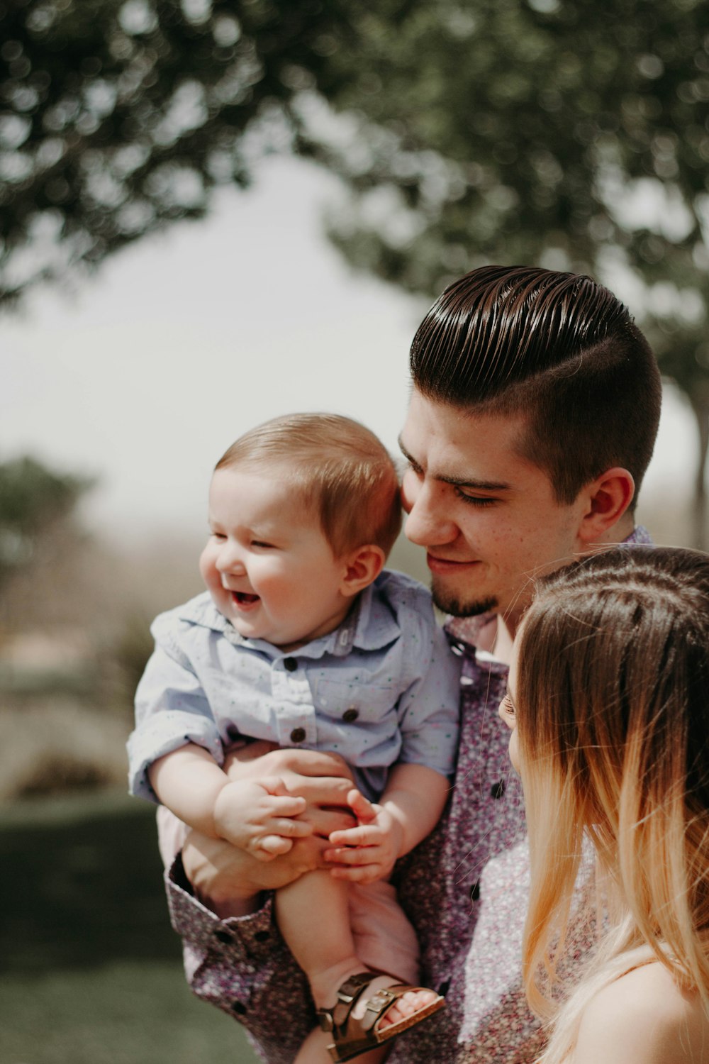 man carrying baby beside woman while smiling to each other