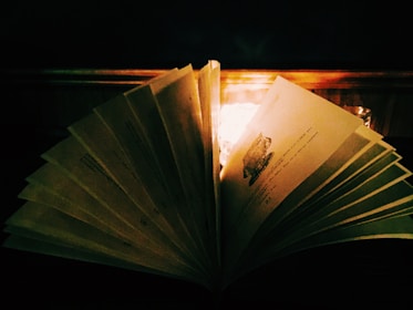 Open book with glowing pages resting on a wooden table, surrounded by candles.