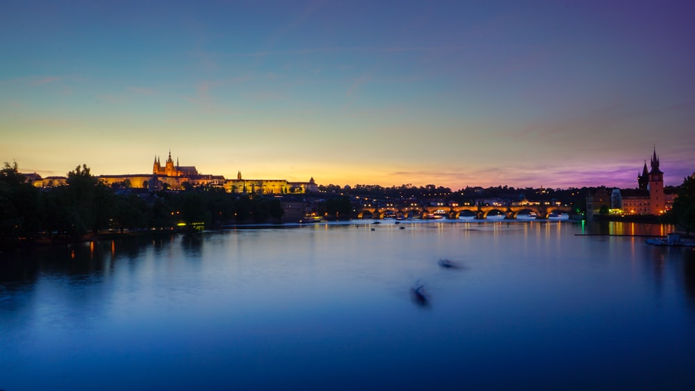 silhouette of city between calm water and golden sky