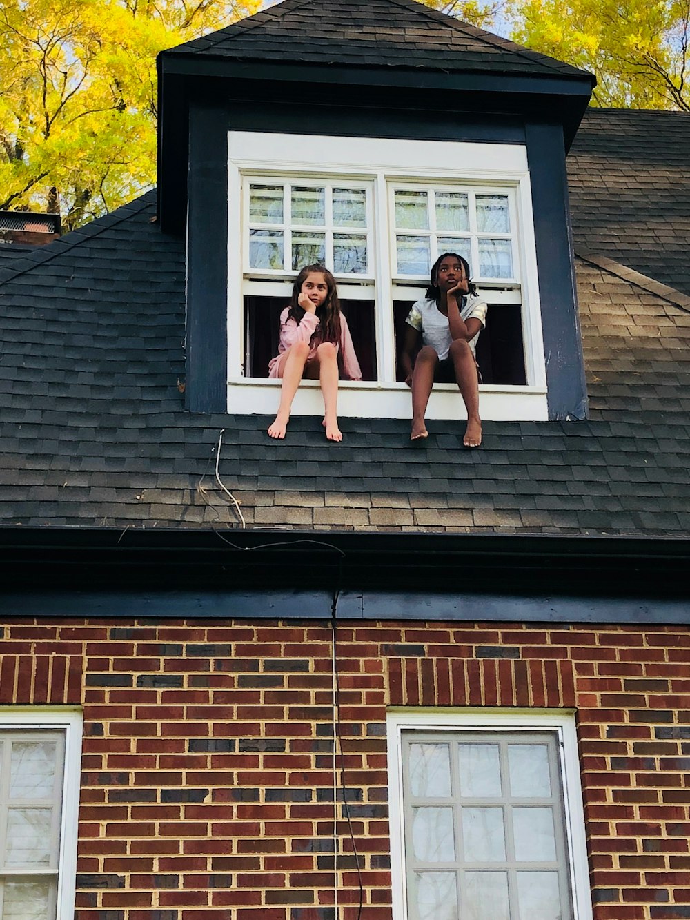 two girls sitting on white 2-panel windows during daytime
